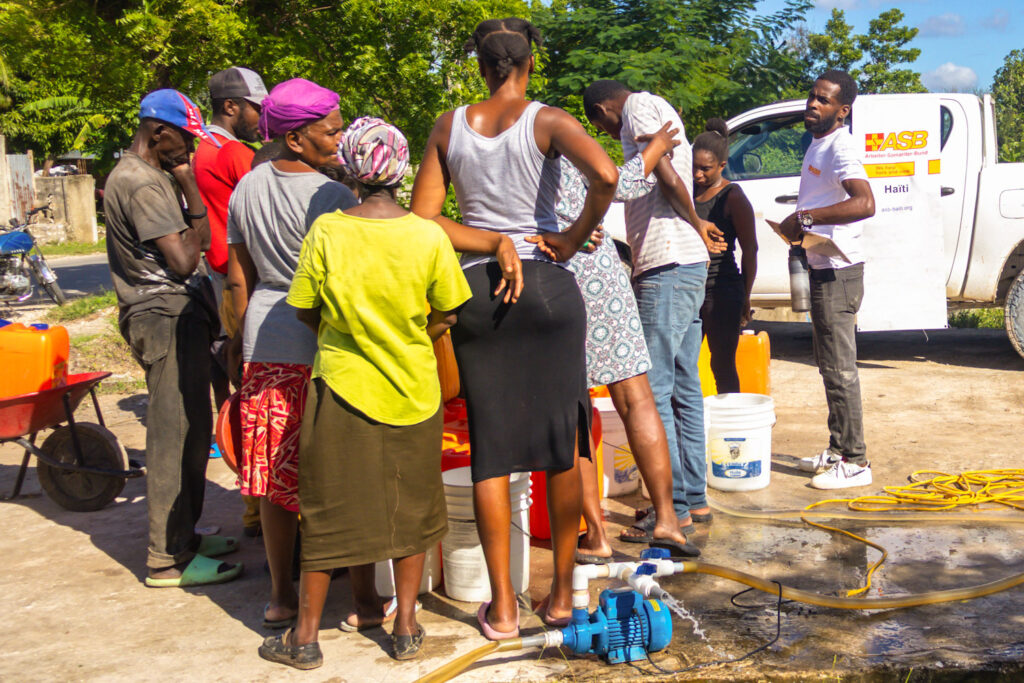 Des habitants remplissent des récipients pendant une opération de traitement et de distribution d’eau organisée par ASB à Camp-Perrin après l’ouragan Melissa.